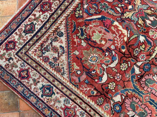 fig 1. A hand-knotted antique Persian Mahal carpet featuring a terracotta red field with intricate floral motifs surrounded by cream and navy decorative borders.