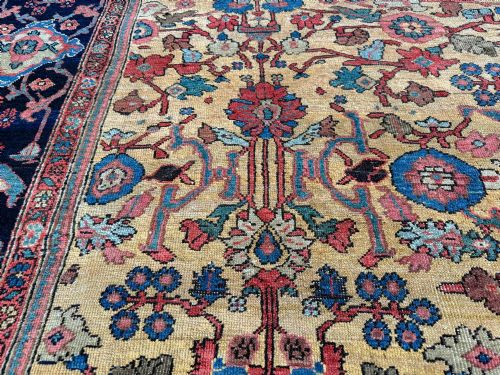 fig 1. An antique Farahan Persian wool carpet with a yellow floral field framed by a dark navy decorative border.