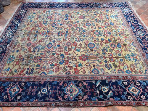 fig 3. An antique Farahan Persian wool carpet with a yellow floral field framed by a dark navy decorative border.