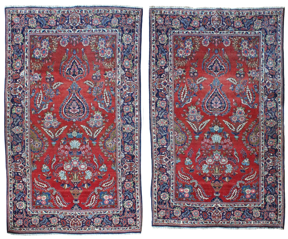 A pair of hand-knotted antique Persian Kashan rugs featuring crimson red fields decorated with floral urns and teardrop motifs within dark navy blue borders.