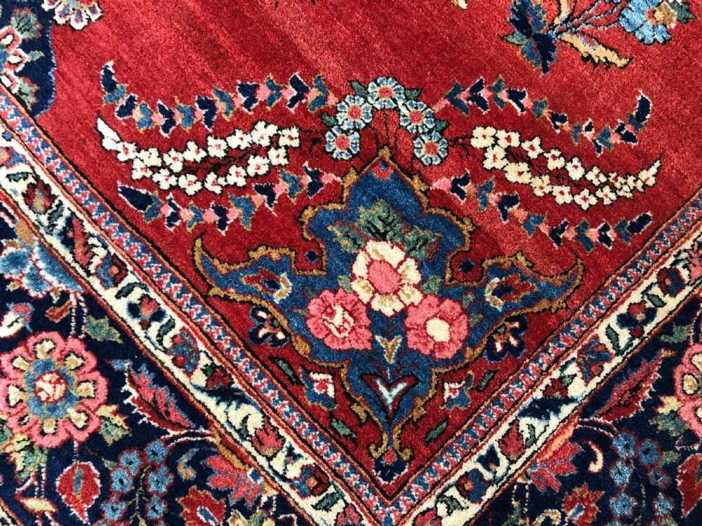A pair of hand-knotted antique Persian Kashan rugs featuring crimson red fields decorated with floral urns and teardrop motifs within dark navy blue borders. View II