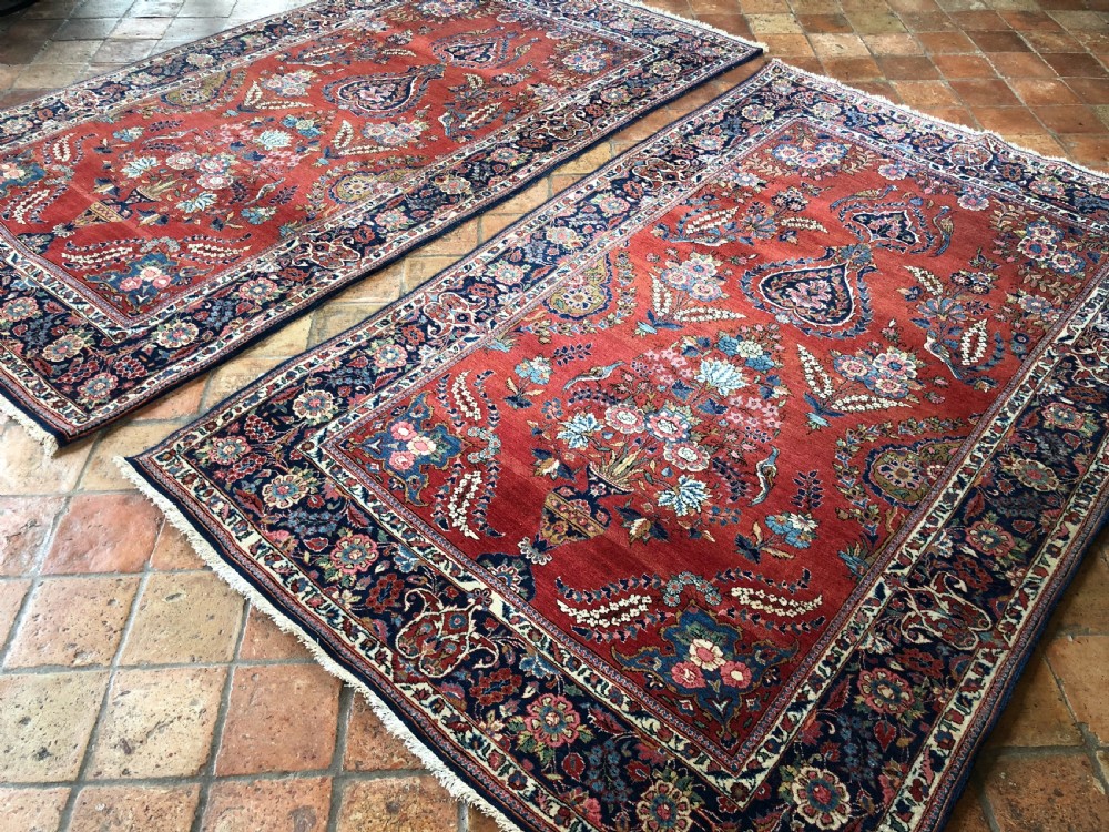 A pair of hand-knotted antique Persian Kashan rugs featuring crimson red fields decorated with floral urns and teardrop motifs within dark navy blue borders. View IV