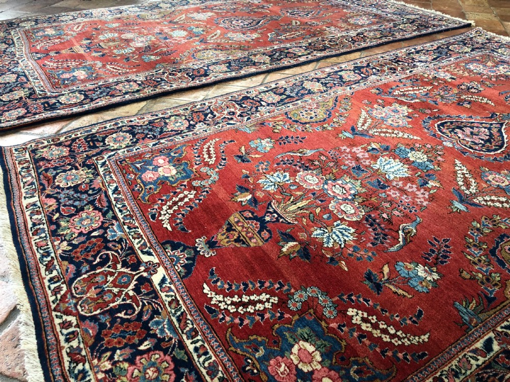 A pair of hand-knotted antique Persian Kashan rugs featuring crimson red fields decorated with floral urns and teardrop motifs within dark navy blue borders. View V