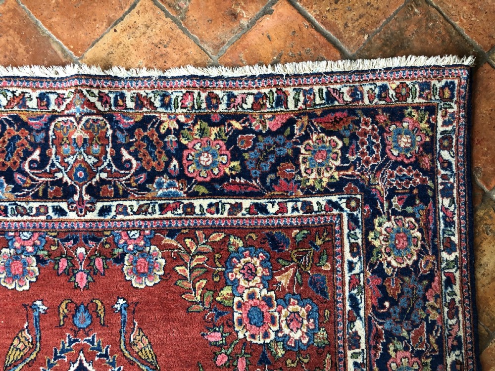 A pair of hand-knotted antique Persian Kashan rugs featuring crimson red fields decorated with floral urns and teardrop motifs within dark navy blue borders. View VI