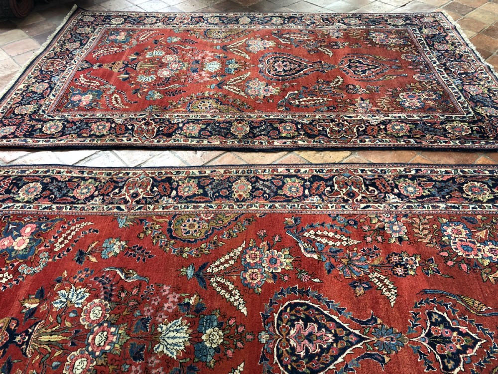 A pair of hand-knotted antique Persian Kashan rugs featuring crimson red fields decorated with floral urns and teardrop motifs within dark navy blue borders. View IX