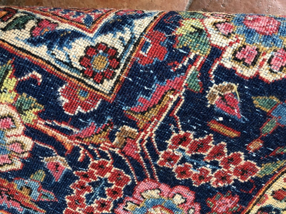A pair of hand-knotted antique Persian Kashan rugs featuring crimson red fields decorated with floral urns and teardrop motifs within dark navy blue borders. View X