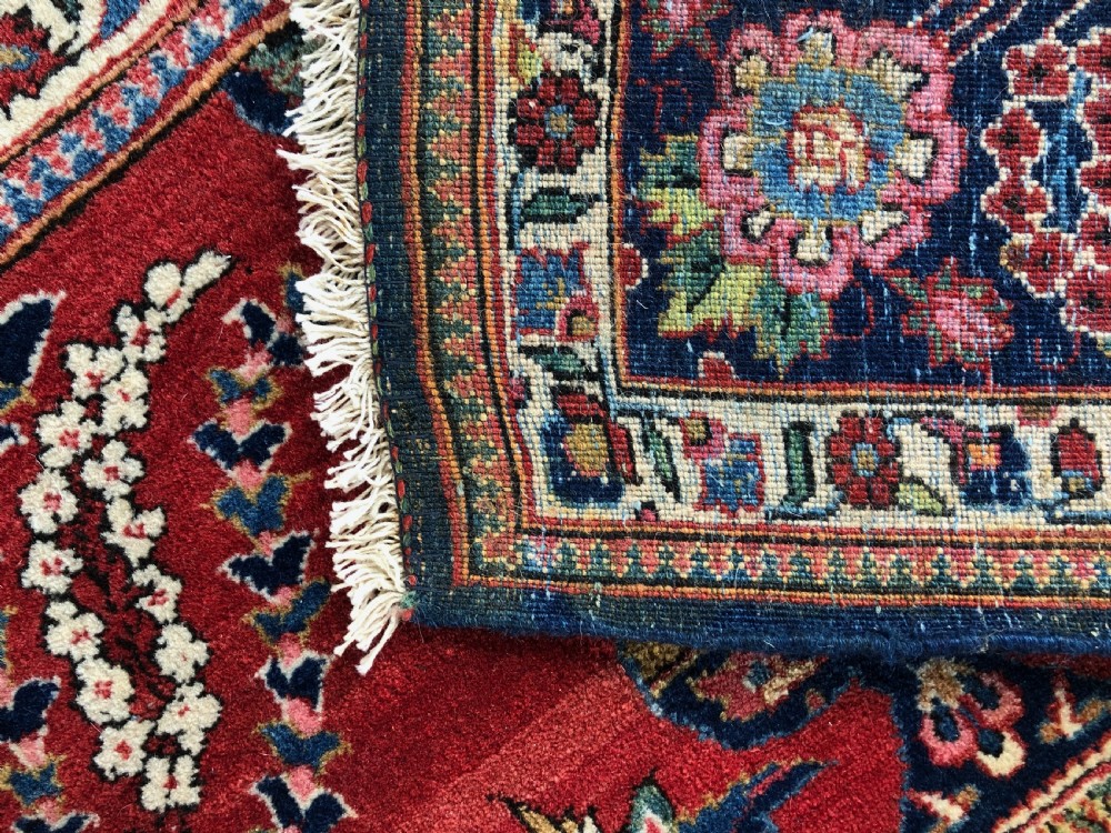 A pair of hand-knotted antique Persian Kashan rugs featuring crimson red fields decorated with floral urns and teardrop motifs within dark navy blue borders. View XI