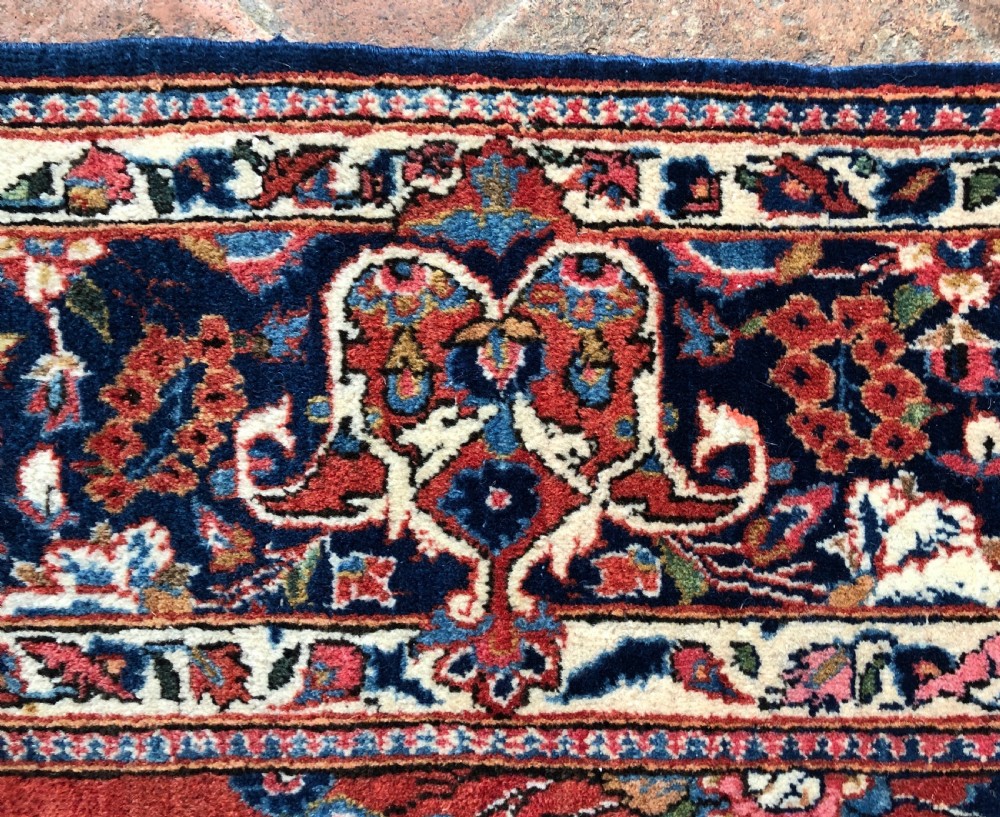 A pair of hand-knotted antique Persian Kashan rugs featuring crimson red fields decorated with floral urns and teardrop motifs within dark navy blue borders. View XIV