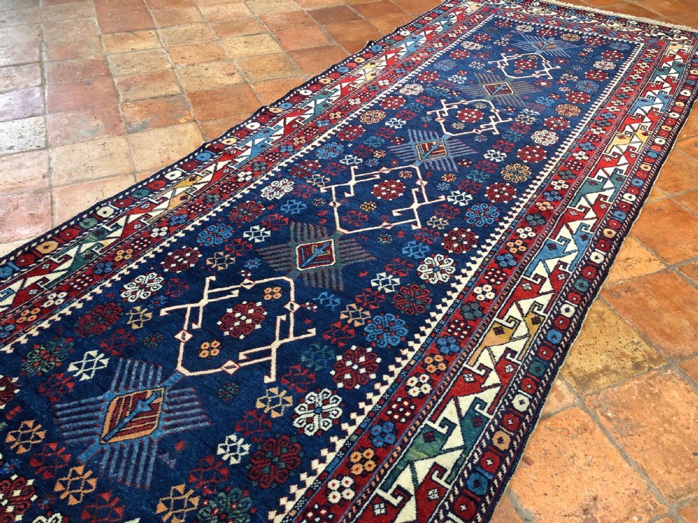 An antique hand-knotted wool runner rug featuring a deep navy field filled with geometric diamond medallions, stylized floral motifs, and multi-coloured geometric borders. View III