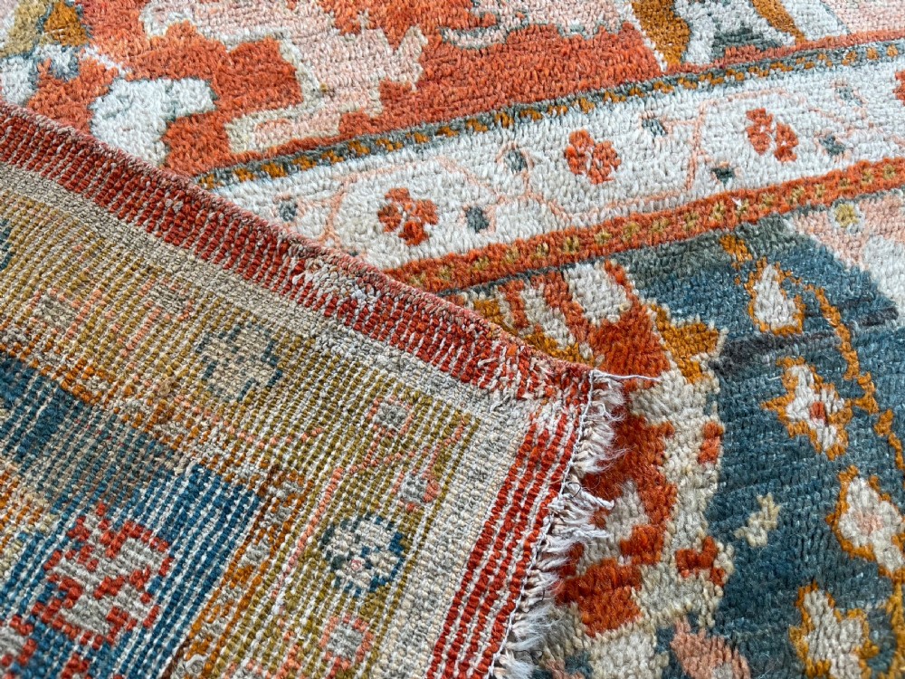 An antique hand-knotted Ushak wool carpet featuring a terracotta central field with stylised ivory medallions and a dark blue border. View II