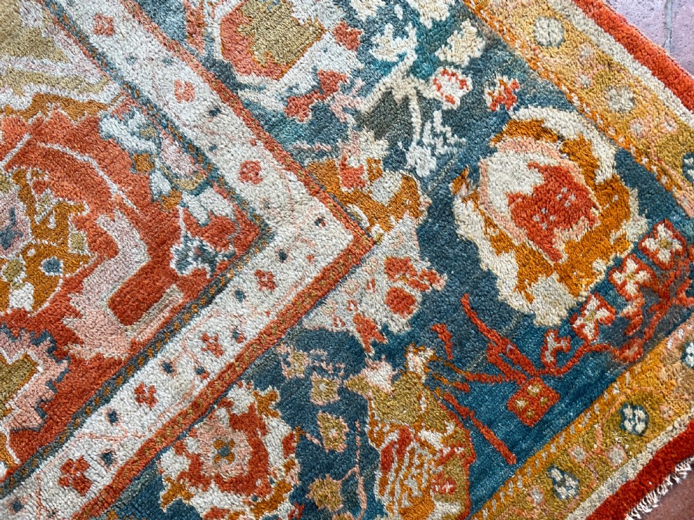 An antique hand-knotted Ushak wool carpet featuring a terracotta central field with stylised ivory medallions and a dark blue border. View III