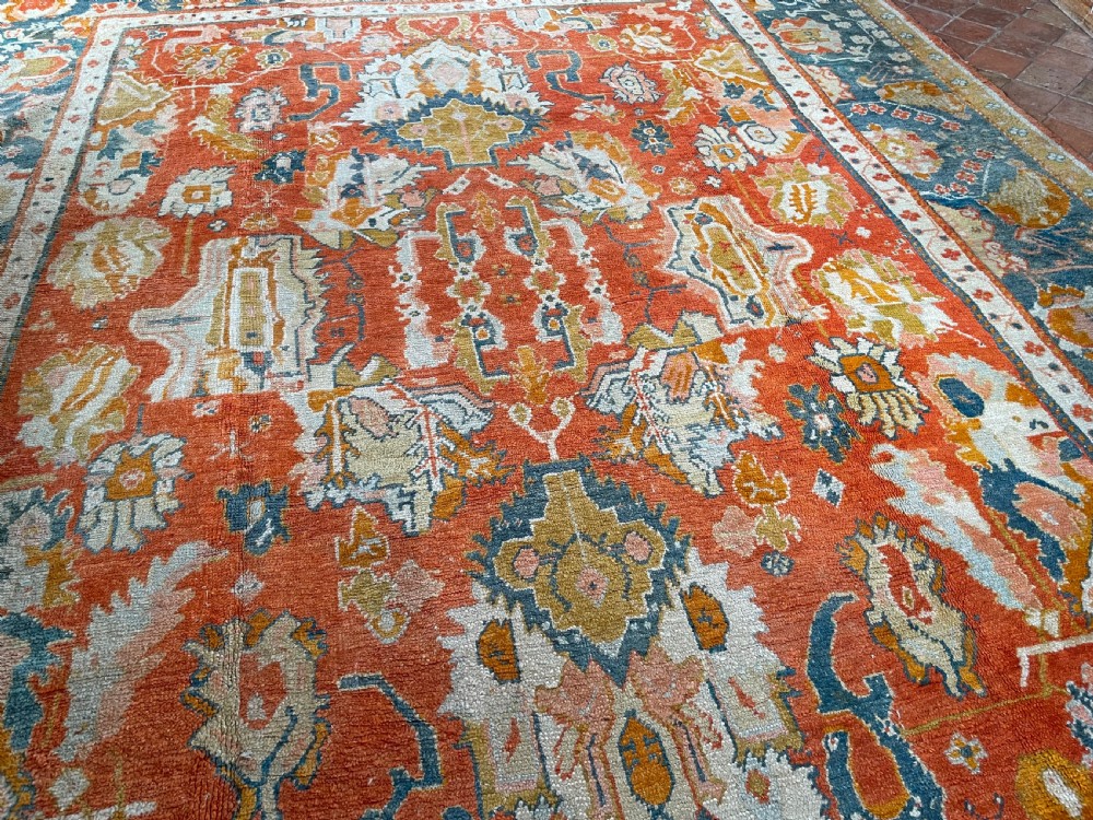 An antique hand-knotted Ushak wool carpet featuring a terracotta central field with stylised ivory medallions and a dark blue border. View IV