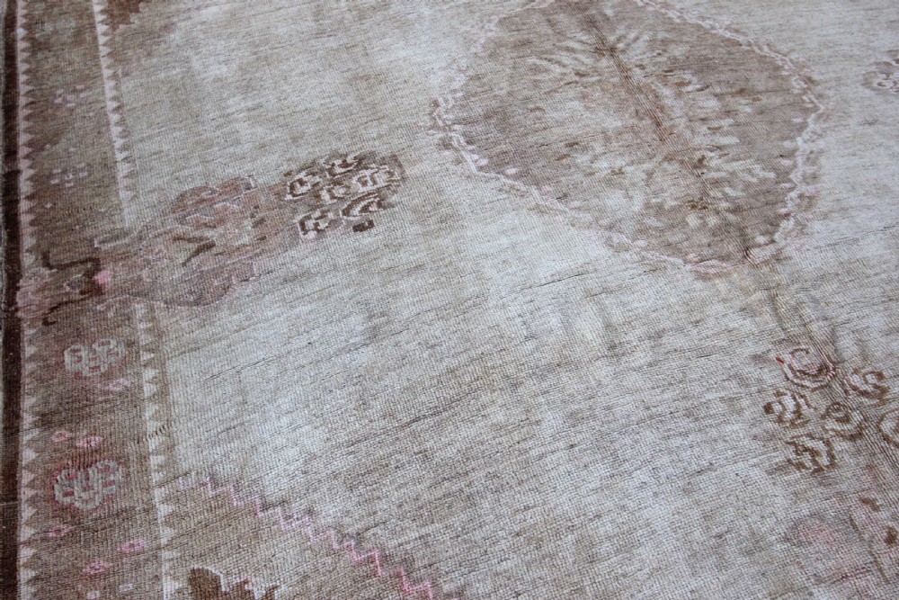An antique Anatolian Ushak wool carpet featuring a central stepped diamond medallion in muted beige, light brown, and soft pink tones with a decorative border. View II