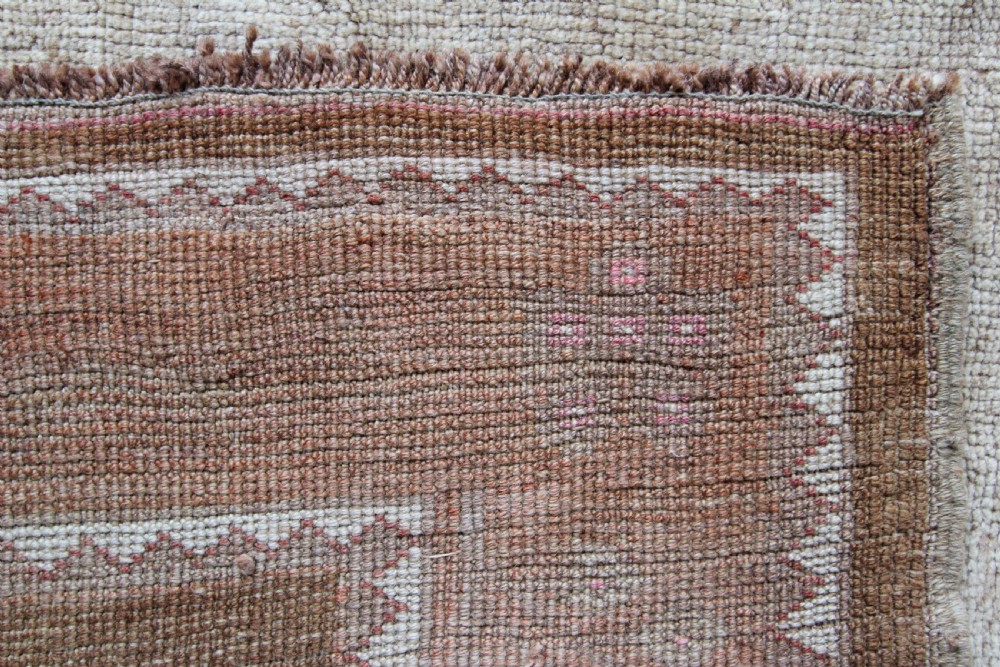 An antique Anatolian Ushak wool carpet featuring a central stepped diamond medallion in muted beige, light brown, and soft pink tones with a decorative border. View IV
