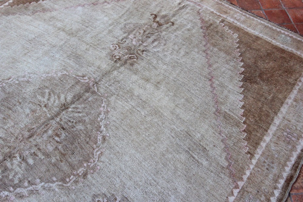 An antique Anatolian Ushak wool carpet featuring a central stepped diamond medallion in muted beige, light brown, and soft pink tones with a decorative border. View V