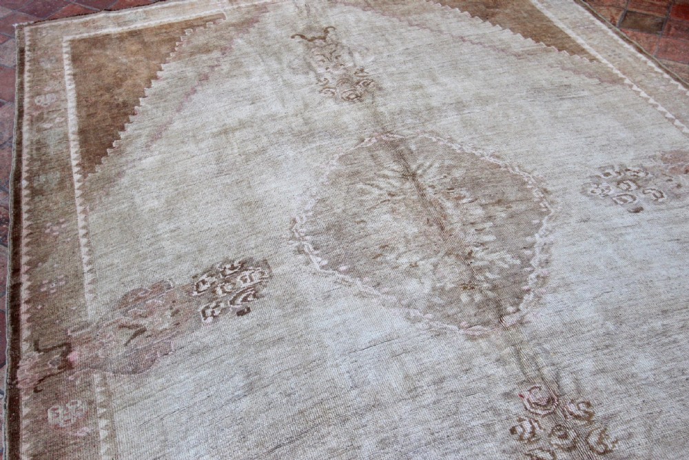An antique Anatolian Ushak wool carpet featuring a central stepped diamond medallion in muted beige, light brown, and soft pink tones with a decorative border. View VI
