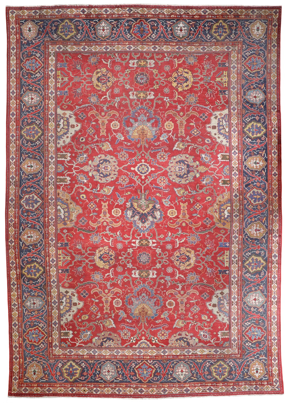 An antique Persian Ziegler carpet featuring a bright red central field with scrolling floral motifs, surrounded by a dark navy blue decorative border.
