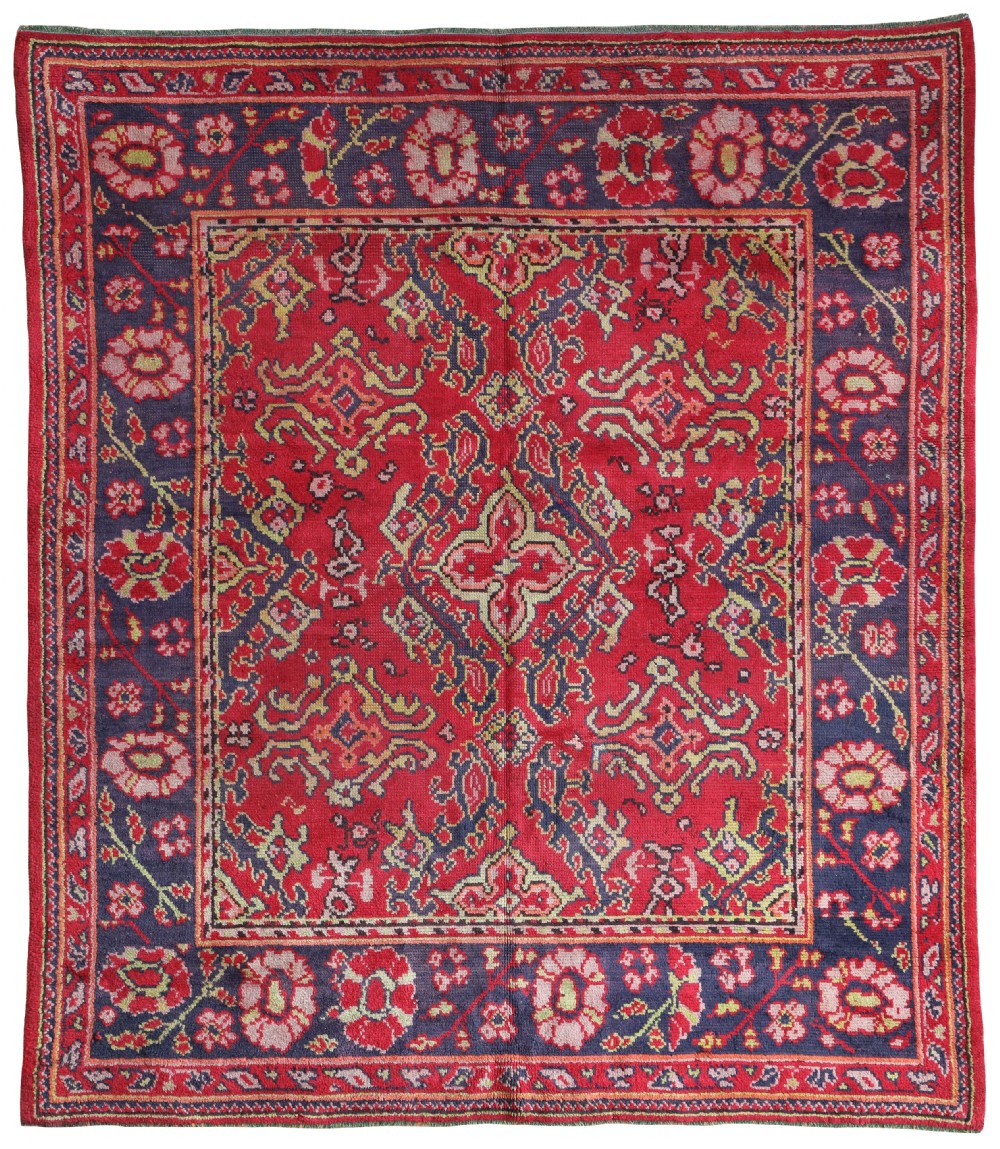 An antique rectangular hand-knotted wool Donegal carpet featuring a red central field decorated with Ushak geometric motifs surrounded by a navy floral border.