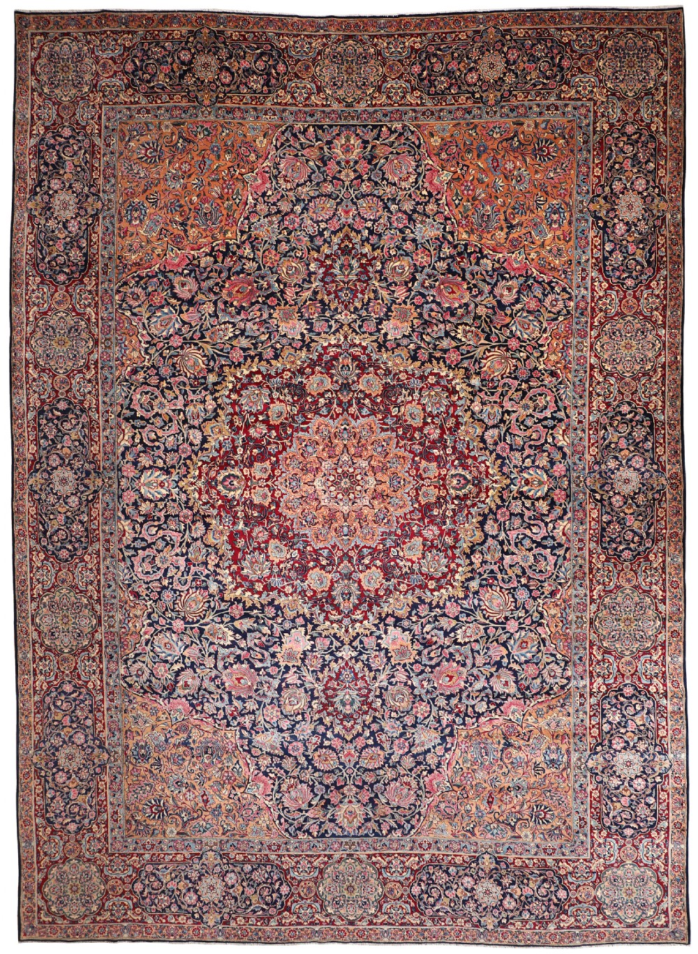 A large rectangular vintage Kirman carpet featuring an intricate central floral medallion, elaborate floral spandrels, and multi-layered decorative borders in tones of red, navy blue, soft pink, and ochre.