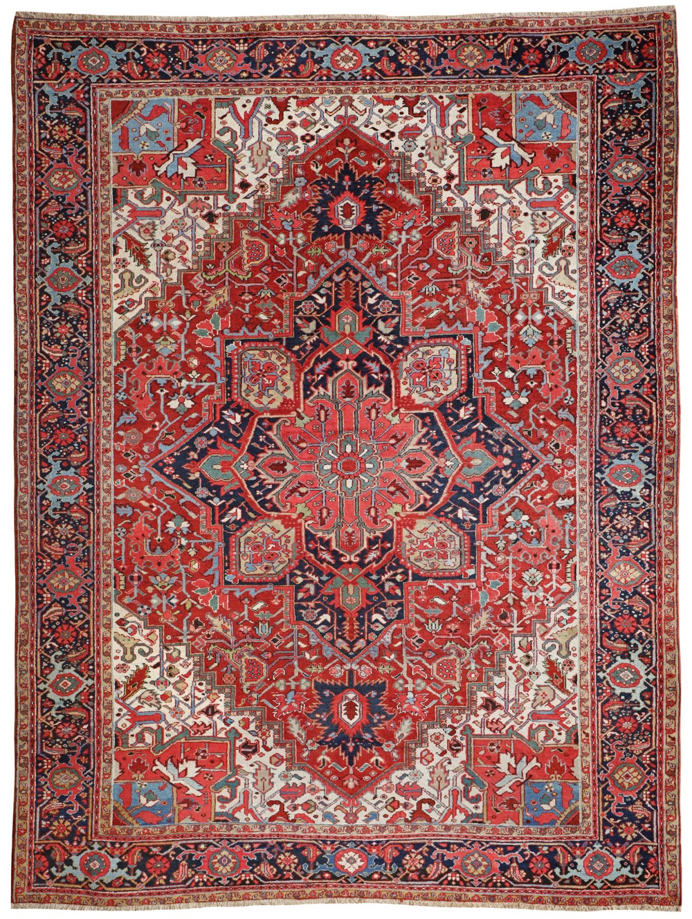 An antique hand-knotted Persian Heriz wool carpet featuring a large geometric central medallion in navy blue and light blue over a terracotta red field with detailed floral borders.