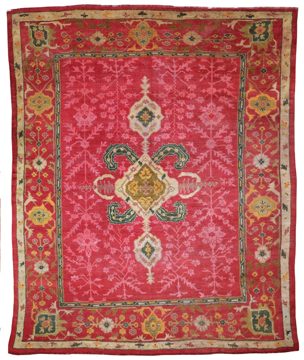 A hand-knotted antique red Ushak carpet featuring a central geometric medallion and floral borders in cream, gold, and green tones.