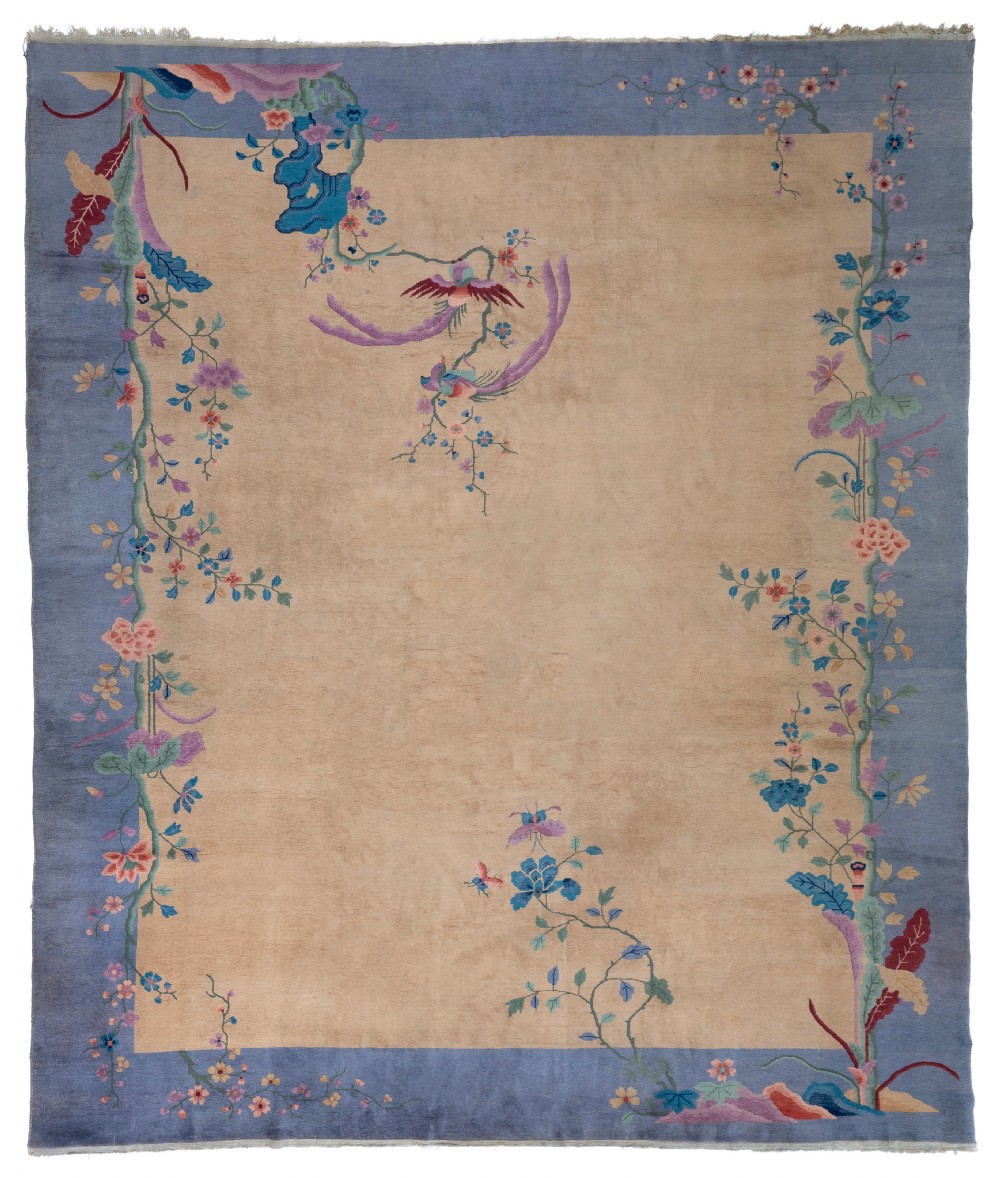 A rectangular Chinese Art Deco wool carpet featuring a beige central field bordered in periwinkle blue with asymmetrical floral and bird motifs.