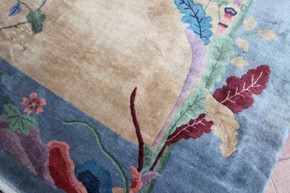 A rectangular Chinese Art Deco wool carpet featuring a beige central field bordered in periwinkle blue with asymmetrical floral and bird motifs. View IV