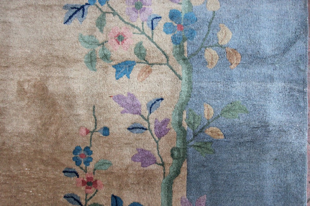 A rectangular Chinese Art Deco wool carpet featuring a beige central field bordered in periwinkle blue with asymmetrical floral and bird motifs. View V