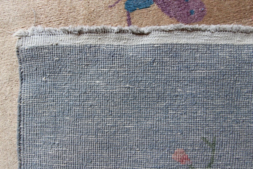 A rectangular Chinese Art Deco wool carpet featuring a beige central field bordered in periwinkle blue with asymmetrical floral and bird motifs. View VI