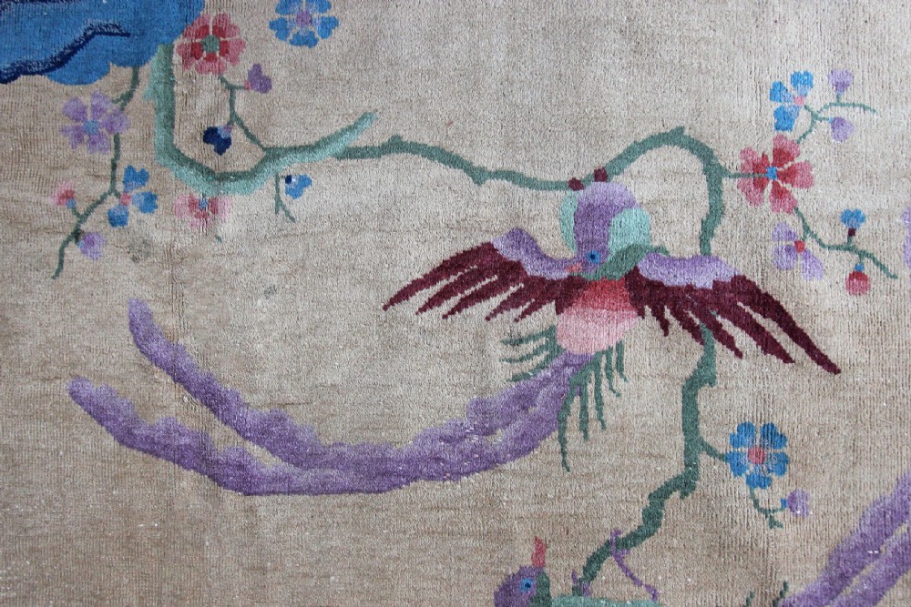 A rectangular Chinese Art Deco wool carpet featuring a beige central field bordered in periwinkle blue with asymmetrical floral and bird motifs. View VII