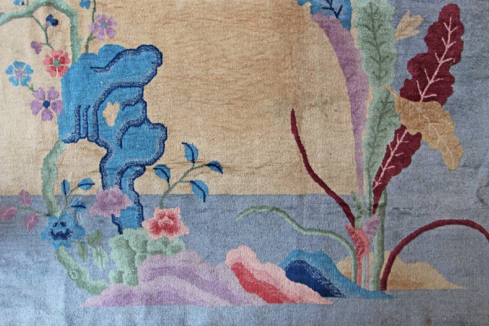 A rectangular Chinese Art Deco wool carpet featuring a beige central field bordered in periwinkle blue with asymmetrical floral and bird motifs. View VIII
