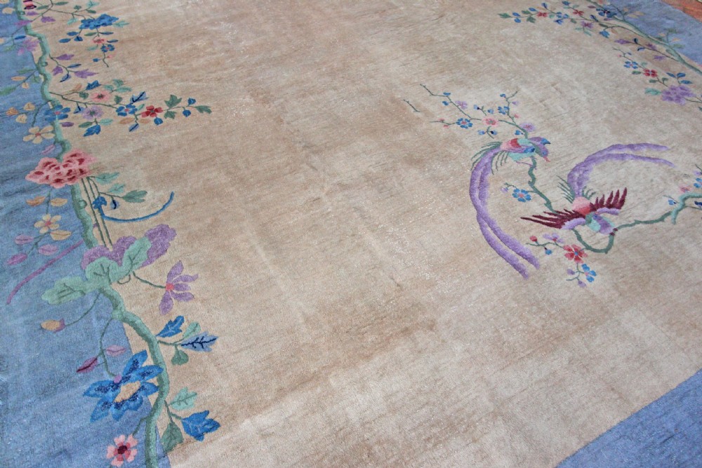 A rectangular Chinese Art Deco wool carpet featuring a beige central field bordered in periwinkle blue with asymmetrical floral and bird motifs. View IX