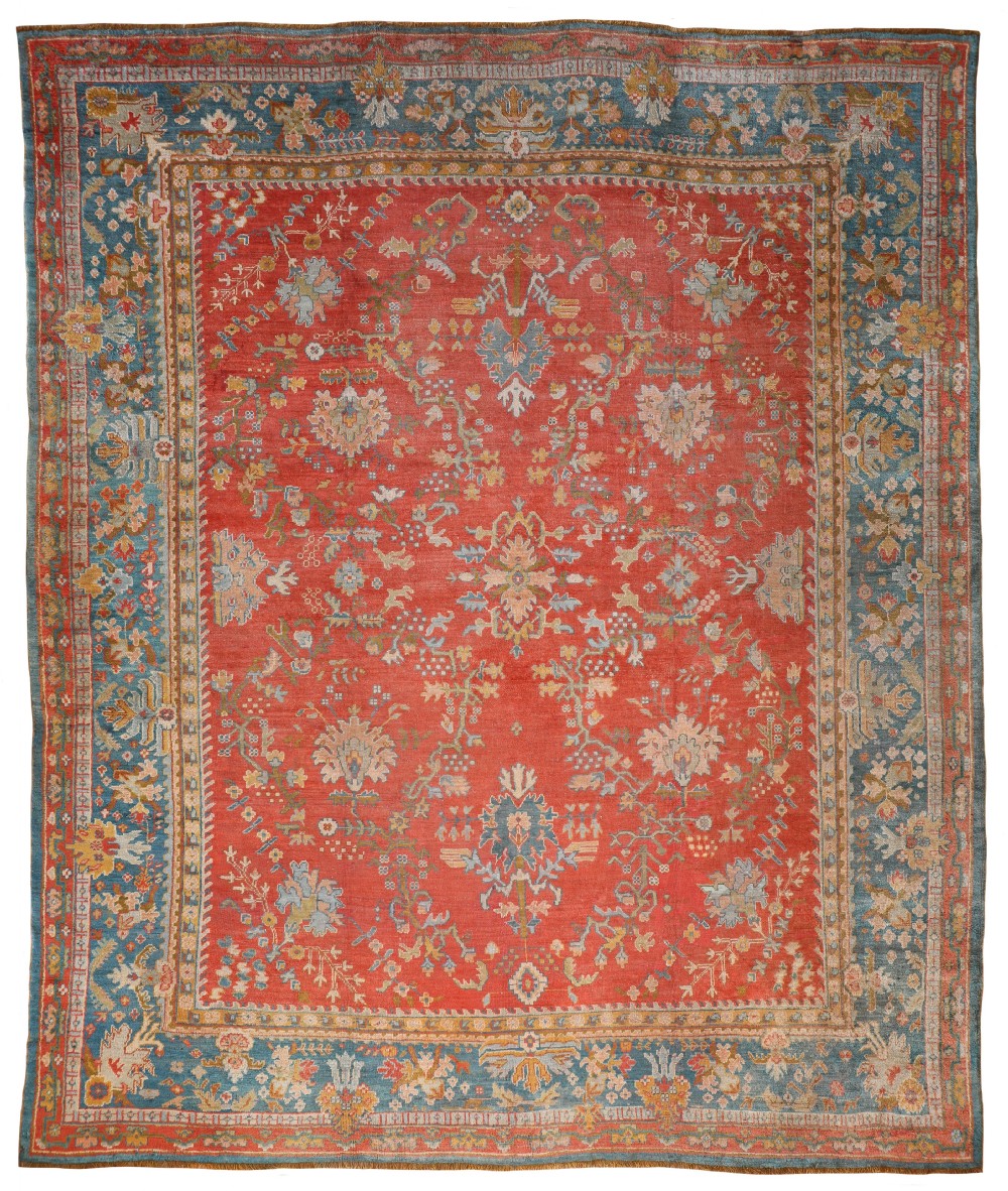 A large hand-knotted Ushak wool carpet featuring a terracotta red field filled with intricate floral motifs and a contrasting blue palmette border.