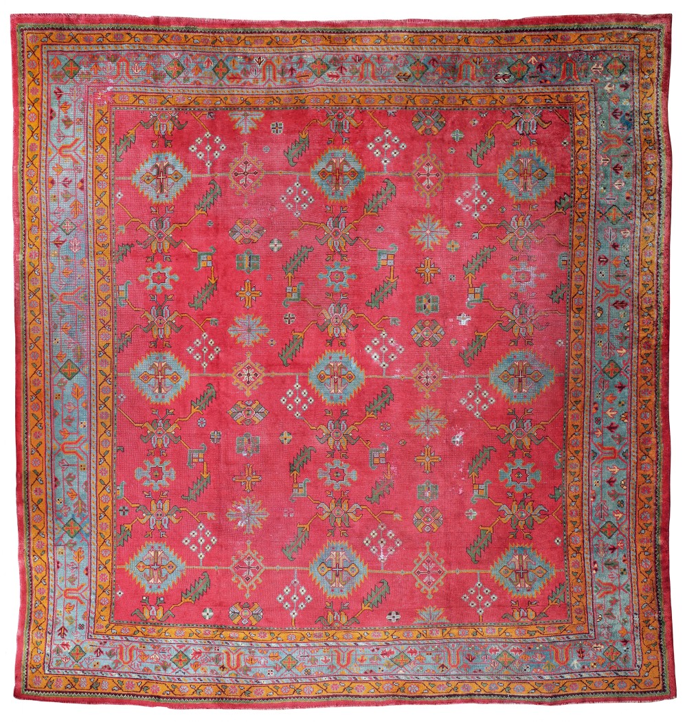 A square hand-knotted Turkish Ushak carpet featuring a magenta centre field adorned with repeating geometric medallions and enclosed by a multi-tiered blue and orange floral border.
