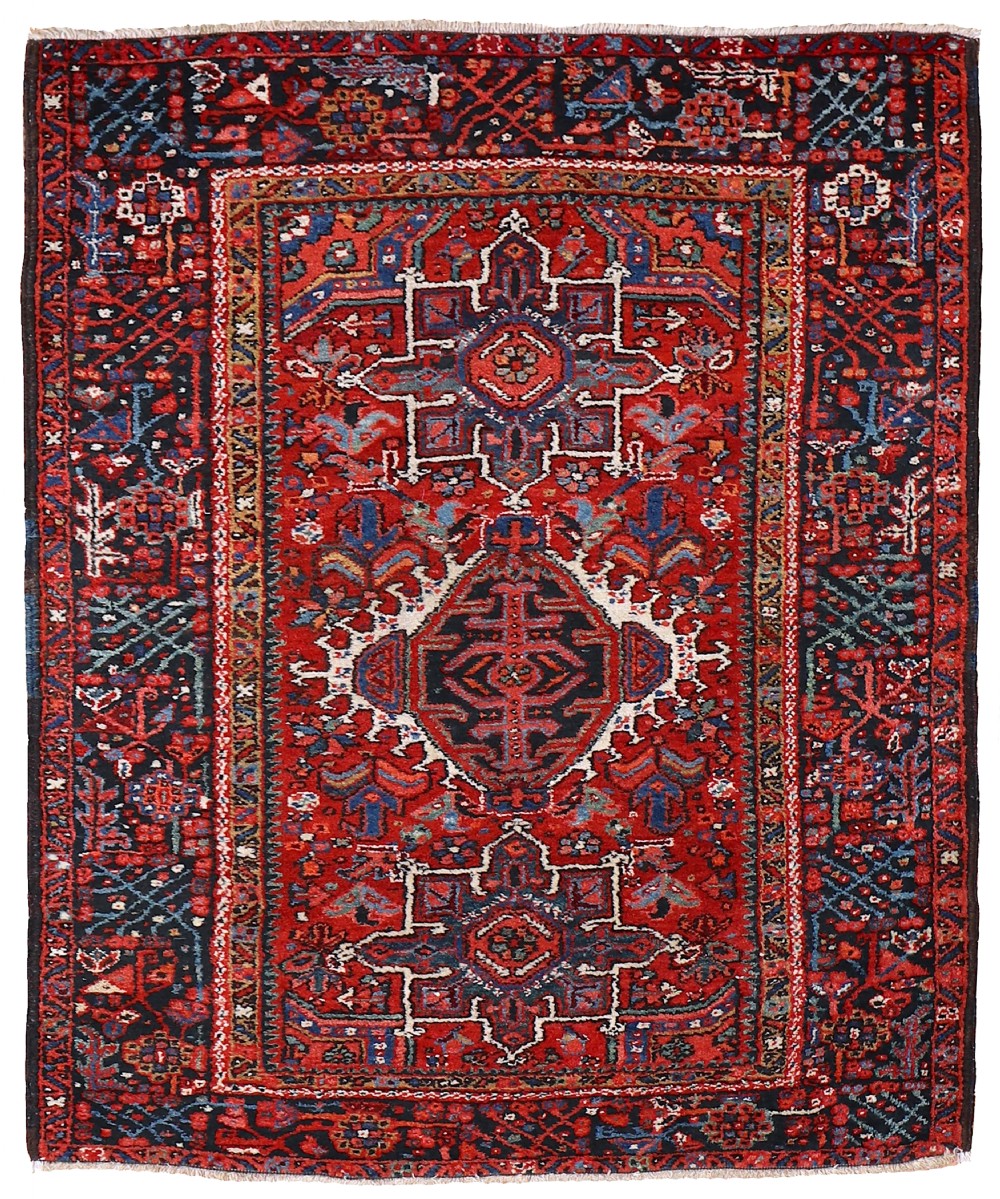 A hand-knotted antique Karaja wool rug featuring a deep red field decorated with geometric central medallions in navy blue, ivory, and terracotta, enclosed within a dark patterned border.