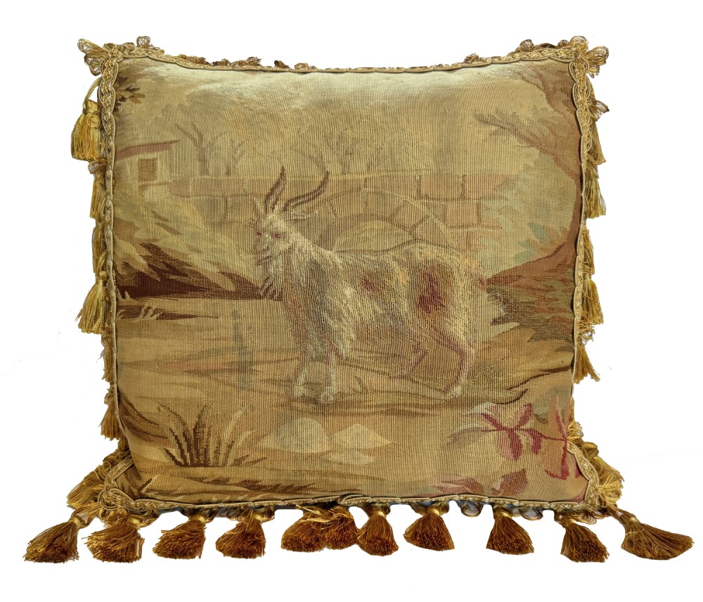 A square antique Aubusson tapestry cushion featuring a pastoral scene with a goat, framed with gold tassels.