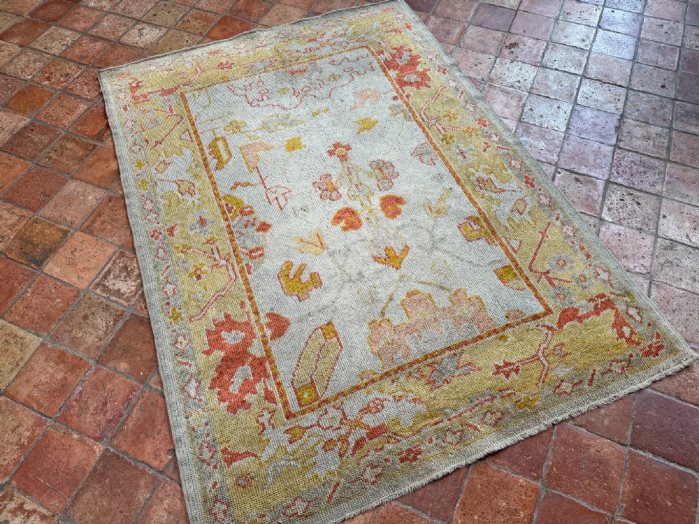 An antique Ushak wool rug featuring a cream central field with muted orange and yellow floral motifs framed by a wide ochre patterned border. View IX