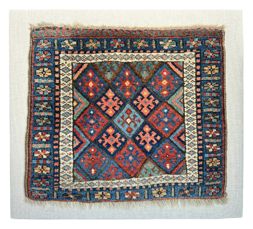 A square antique woven wool Jaf Kurdish bag face featuring geometric diamond lattice patterns in blue, red, ochre, and cream colours.