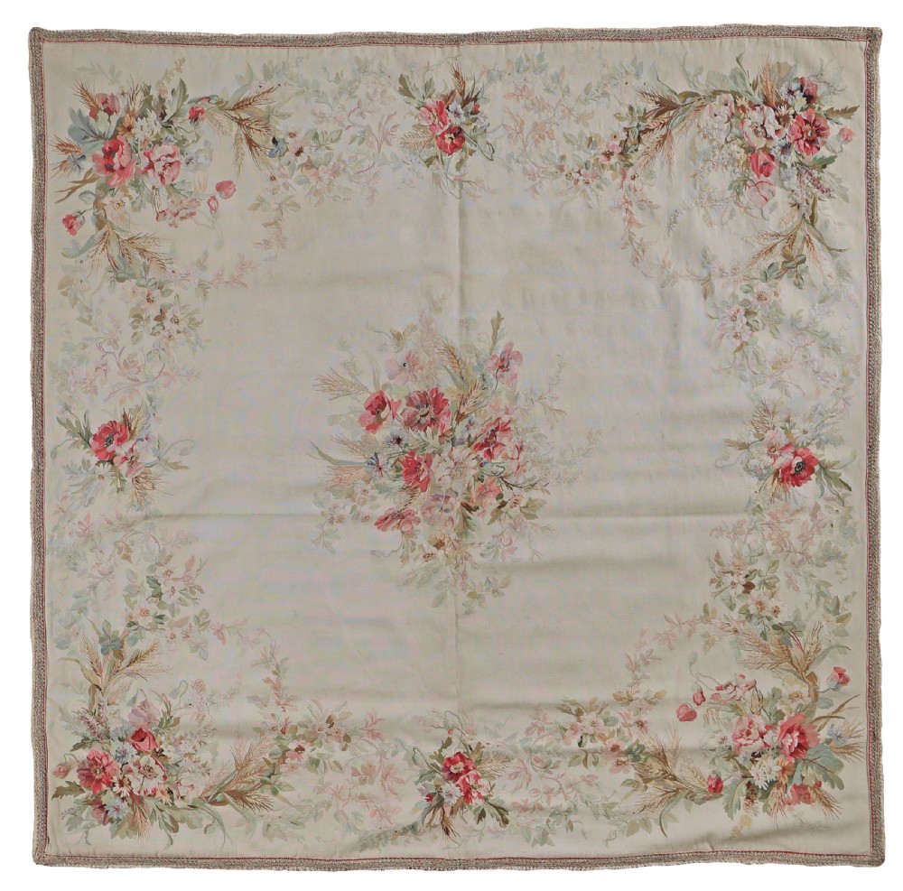 An antique square flatweave Aubusson rug featuring a cream field with a central floral bouquet framed by floral garlands along the border.