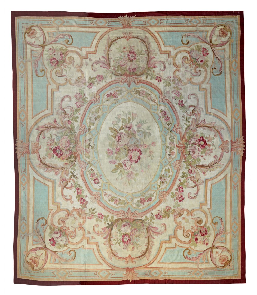 An antique French Aubusson flatweave carpet featuring a central oval floral medallion surrounded by pastel blue panels, pink rose garlands, and ornate scrollwork borders.