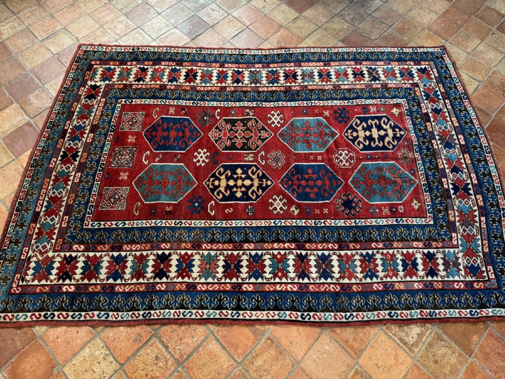 An antique rectangular hand-knotted wool Kazak rug featuring a red field with geometric hexagonal medallions and multi-coloured borders. View II