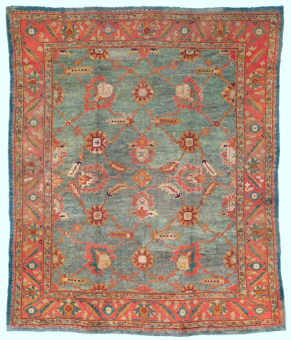 An antique hand-knotted wool Ushak carpet featuring a muted teal field with a lattice of floral palmettes surrounded by a wide terracotta border.