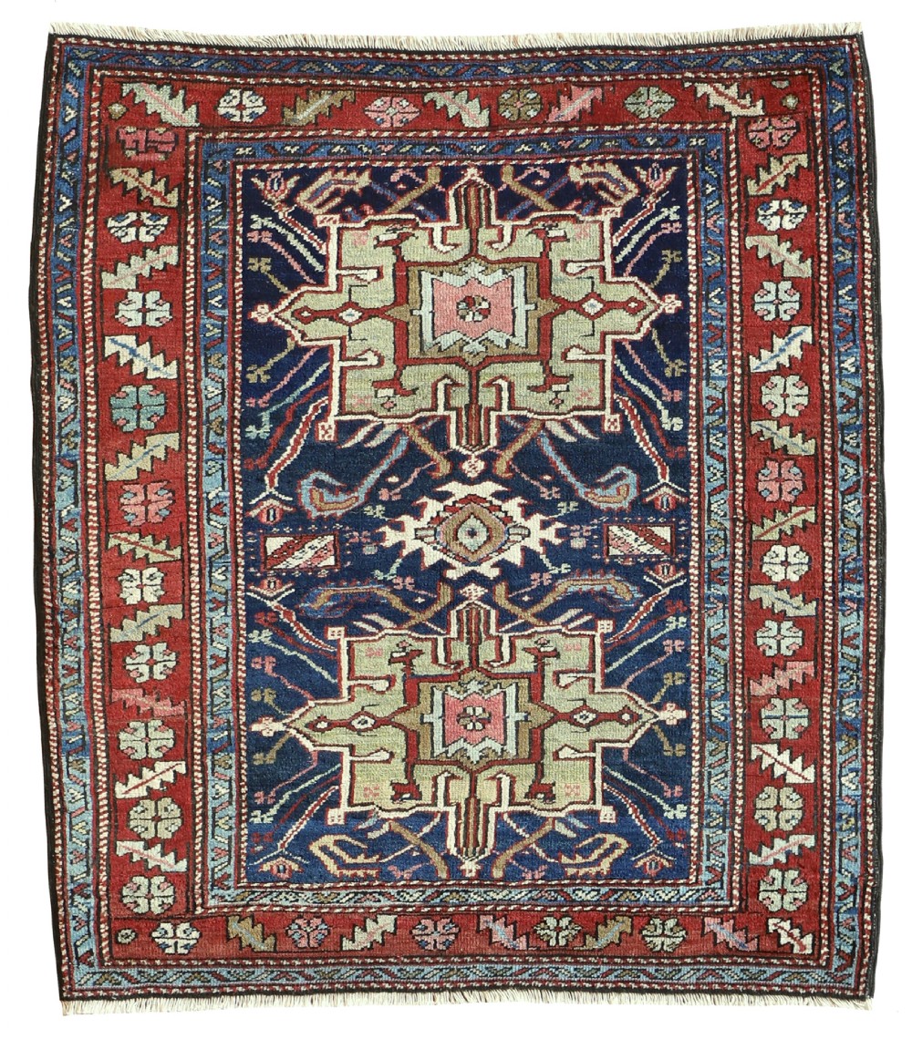 An antique hand-knotted Persian Karaja rug featuring a dark navy central field with geometric stepped medallions and a terracotta red border.