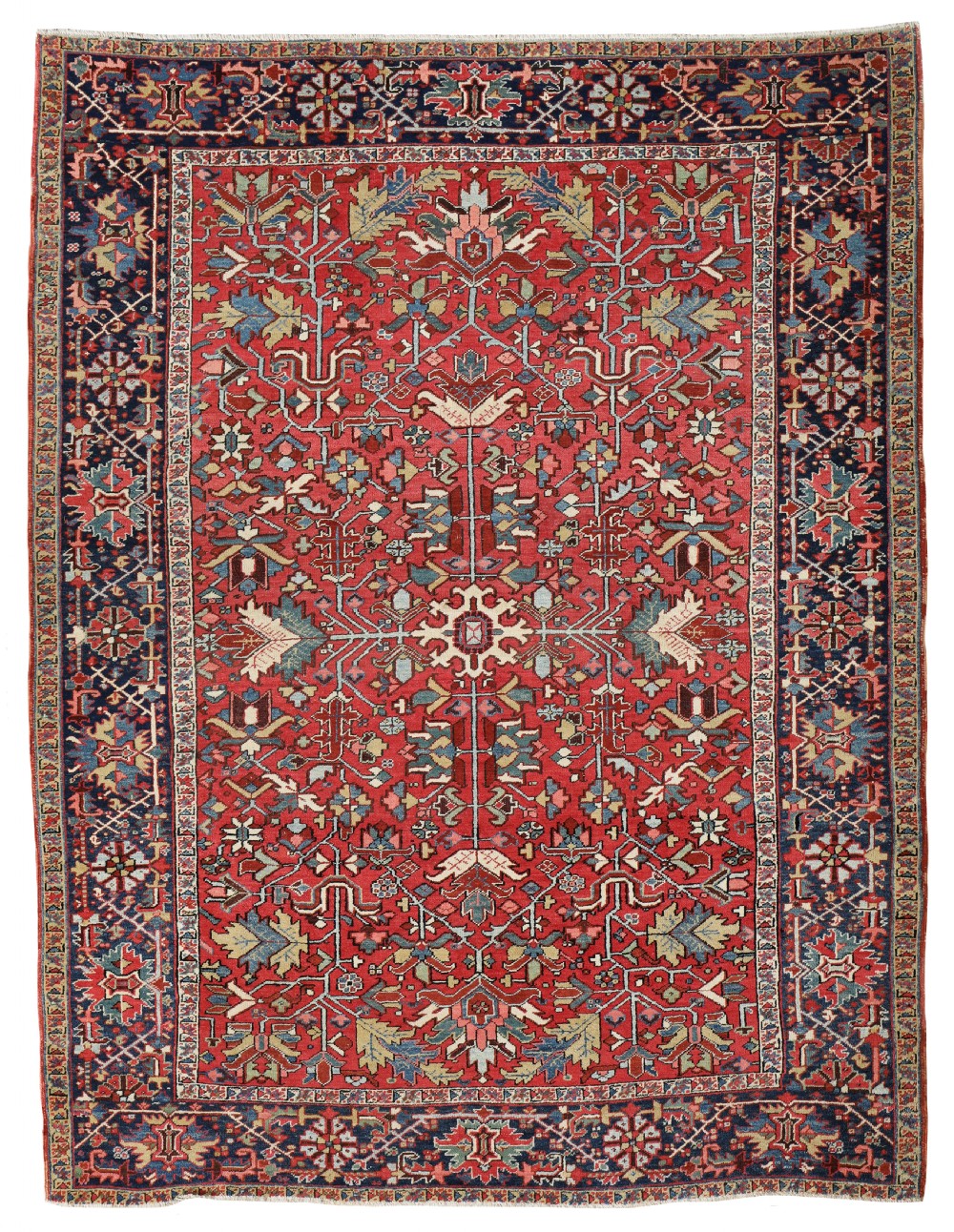 An antique Persian Heriz wool carpet featuring a complex geometric botanical design in terracotta red, navy blue, and soft green tones.