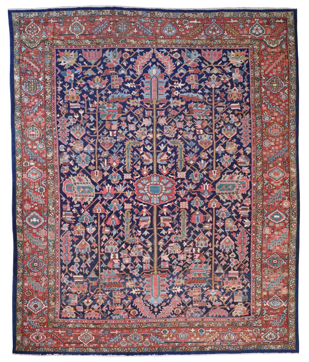 A rectangular hand-knotted antique Heriz carpet featuring a dark navy central field filled with geometric floral motifs and a wide terracotta red border.