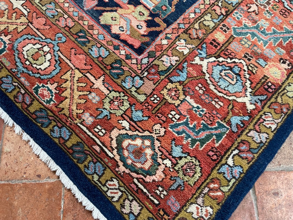 A rectangular hand-knotted antique Heriz carpet featuring a dark navy central field filled with geometric floral motifs and a wide terracotta red border. View II