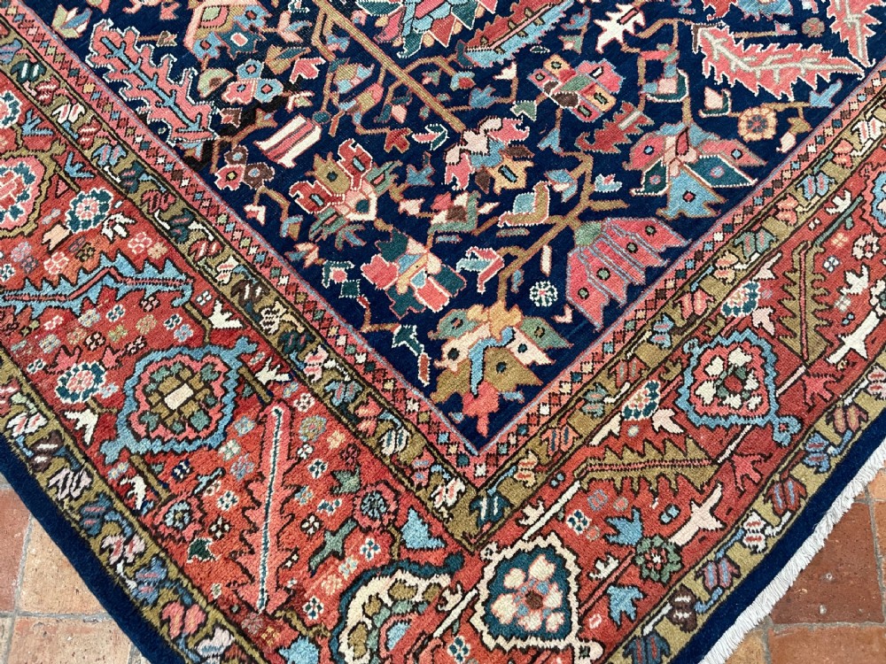 A rectangular hand-knotted antique Heriz carpet featuring a dark navy central field filled with geometric floral motifs and a wide terracotta red border. View IV