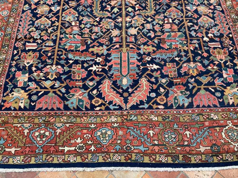 A rectangular hand-knotted antique Heriz carpet featuring a dark navy central field filled with geometric floral motifs and a wide terracotta red border. View VII