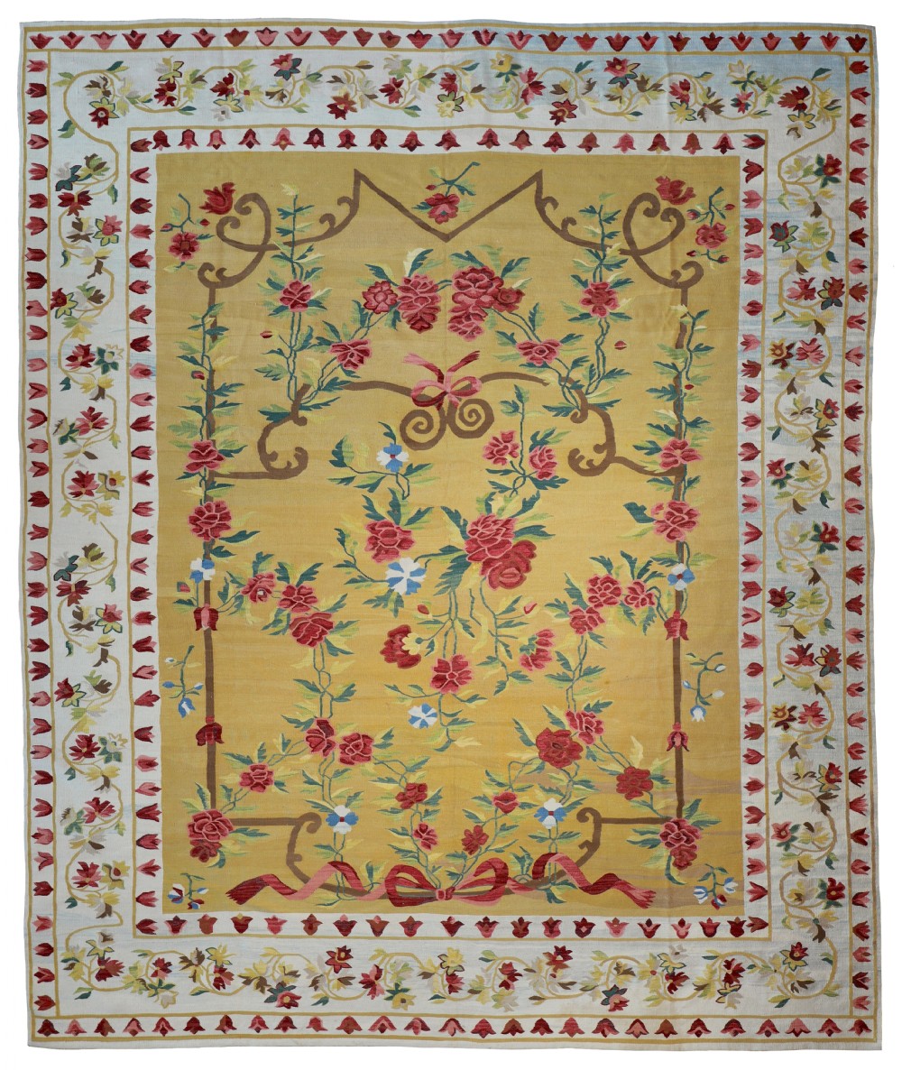 An antique flatweave wool kilim rug featuring a yellow central field adorned with red rose garlands, ribbon bow motifs, and ornate floral borders.