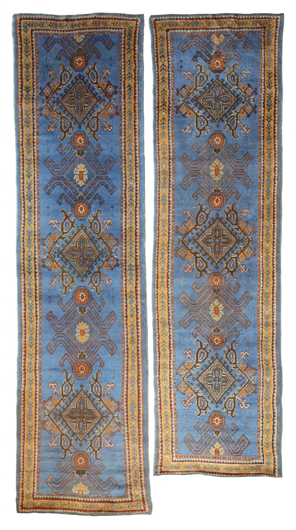 A matching pair of long antique Turkish Ushak wool runner rugs featuring a sky blue background with terracotta and mustard geometric diamond medallions.